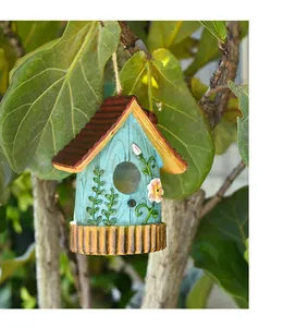Close-up of a blue garden birdhouse with pink flowers hanging on a natural green branch