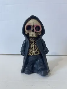 Detail shot of a cute Grim Reaper skull figurine with pink eyes and black hooded resin robe