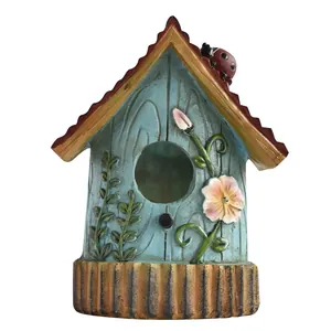 Pastel blue resin birdhouse with pink flower reliefs and a ladybug on a red tile roof