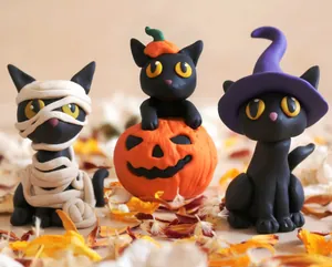 Close-up of three resin Halloween black cat figurines with pumpkin and witch hat decorations