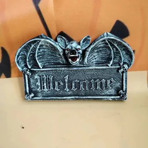 Gothic Halloween welcome sign featuring a winged bat with red eyes on orange pumpkin background