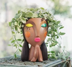 Detail of creative resin girl planter with prayer pose and vibrant hand-painted facial features