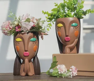 Detail of creative resin face planters featuring vibrant makeup and hand-praising poses