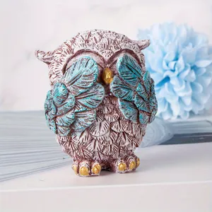 Close-up of a vintage owl resin figurine covering its eyes with blue wings and gold beak