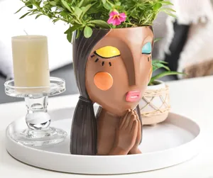 Detail of female face resin planter with blue eyeshadow and floral hair decoration