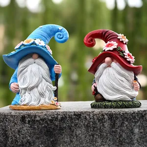 Close-up of hand-painted resin Christmas gnomes with floral hats in a garden setting