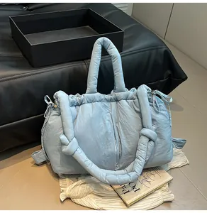 Detailed close-up of light blue quilted puffer tote bag with thick padded strap and ties