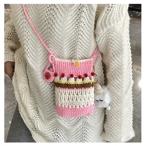 Detailed crochet phone bag with pink strawberry charms worn by a model in white sweater