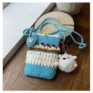 Detail of hand-knitted crossbody bag with cherry decor and fuzzy monster charm