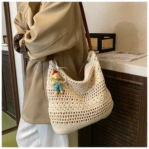 Close-up of cream woven shoulder bag with hollow mesh patterns and cartoon doll charm