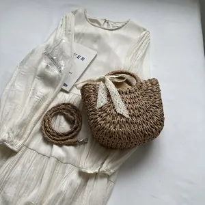Détail d'un sac de plage en paille avec nœud en dentelle blanche et deux poignées