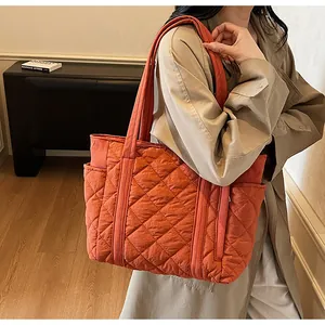 Close-up of orange quilted tote bag with diamond stitching and side pocket on a model