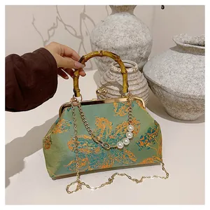 Detail van groene geborduurde tas met bamboe handvat en parelketting van metaal