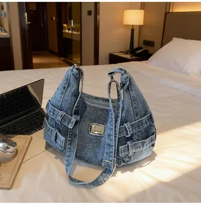 Dettaglio della borsa a tracolla in denim blu lavato con dettagli in metallo su letto bianco