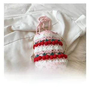 Detailed close-up of handmade pink crochet bucket bag with red cherry accents and label