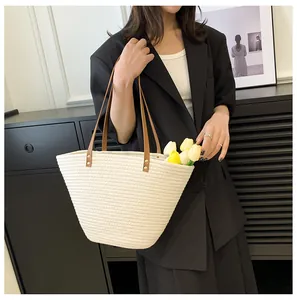 Detail of cream woven tote bag with brown leather handles and gold rivet accents