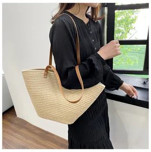 Close-up of a large straw tote bag featuring brown leather shoulder straps and woven texture
