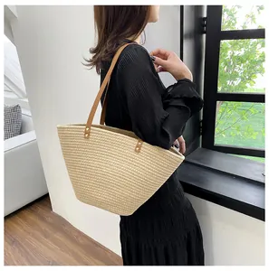 Detail of beige straw tote bag featuring brown leather straps and metal rivet reinforcement
