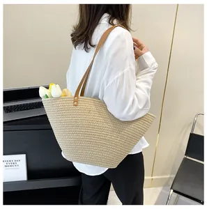 Detail of a large straw tote bag with leather straps showing spacious interior and texture