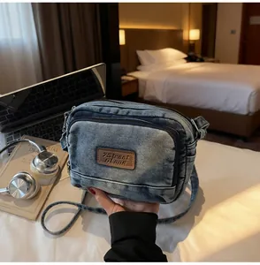 Dettaglio della borsa a tracolla in denim vintage con logo in pelle e tasche a zip