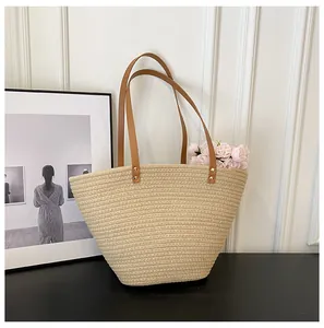 Close-up of woven straw tote bag with brown leather handles and gold metal rivets
