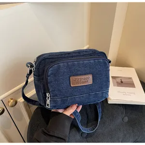 Dettaglio della trama denim blu scuro e della toppa in pelle marrone della borsa a tracolla