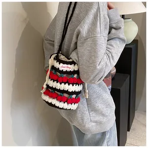 Detail showing hand-knitted drawstring bucket bag with cherry decor and striped texture