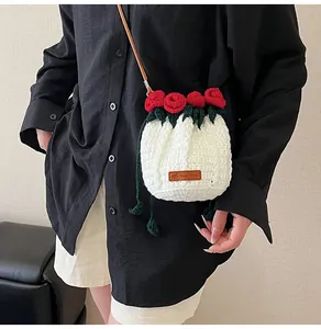 Detail of hand-crocheted white bucket bag featuring red yarn roses and leather strap