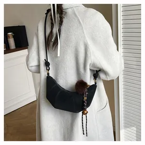 Détail du sac bandoulière noir en croissant avec pompon en fourrure et nœud tressé