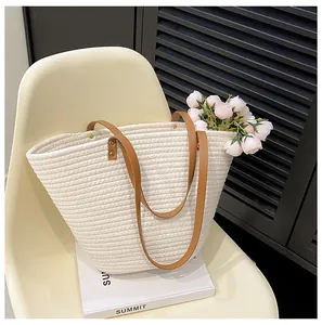 Detail of woven straw tote bag featuring brown leather handles and textured ivory material