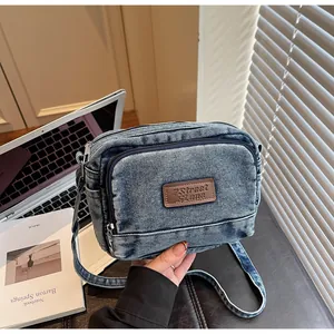 Dettaglio della borsa a tracolla in denim blu con patch logo in pelle marrone e zip metalliche
