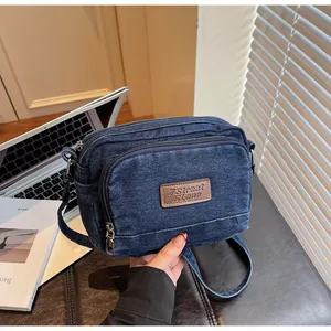 Dettaglio della borsa a tracolla in denim blu scuro con tasche a zip e tracolla regolabile