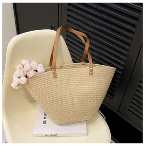 Detail of straw tote bag with brown leather handles and golden rivet reinforcements