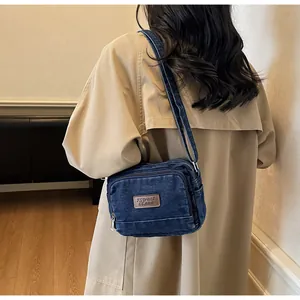 Dettaglio della borsa a tracolla in denim blu con patch in pelle su trench kaki