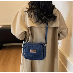 Dettaglio della borsa a tracolla in denim blu con logo in pelle marrone su un trench casual