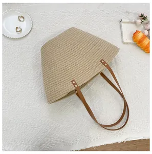 Detail view of woven tote bag with brown leather straps and gold rivets on a flat surface