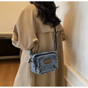 Dettaglio borsa a tracolla in denim lavato con strati di cerniere e toppa in pelle