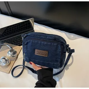 Dettaglio borsa a tracolla in denim blu con doppia zip e toppa in pelle marrone logo