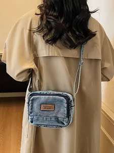 Borsa a tracolla retrò in denim blu indossata su un elegante trench color kaki