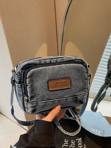 Borsa a tracolla in denim blu lavato con toppa in pelle mostrata in uno specchio