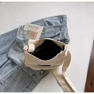 Detailed top view of a minimalist cream canvas crossbody bag on a denim jacket background