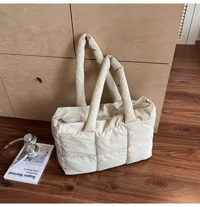 Close-up of cream white quilted puffer tote bag on wooden floor with casual accessories