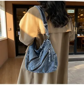 Detail of blue denim tote bag with multiple zippers and long pull tabs in a cafe setting