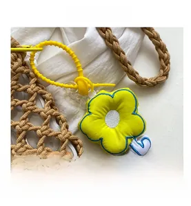 Detail of yellow flower bag charm with blue embroidery and plastic clip on woven bag
