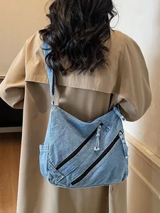 Large blue denim hobo bag with triple front zippers shown on a model in a trench coat
