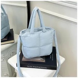 Detail of light blue quilted down tote bag with square texture and dual straps on books