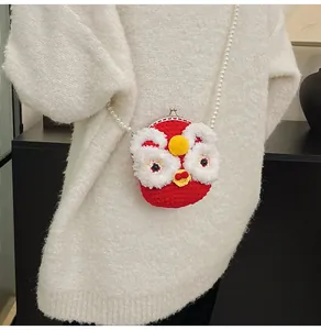 Dettaglio mini borsa rossa a maglia danza del leone con tracolla di perle su maglione bianco