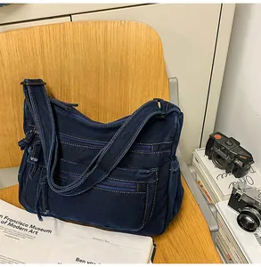 Detail of a vintage dark blue denim messenger bag with multiple pockets on a wooden chair