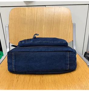 Detail of dark blue denim crossbody bag with contrast stitching on wooden surface