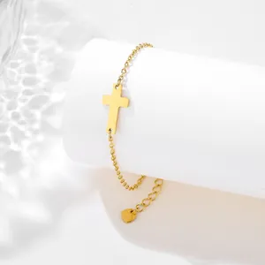 Detailed macro view of a gold cross pendant bracelet with heart charm on a white pedestal